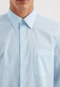 Lichtblauw button-up shirt met een geruit patroon, een klein zakje op de linkerborst en een klassieke kraag. Glad stoftextuur.