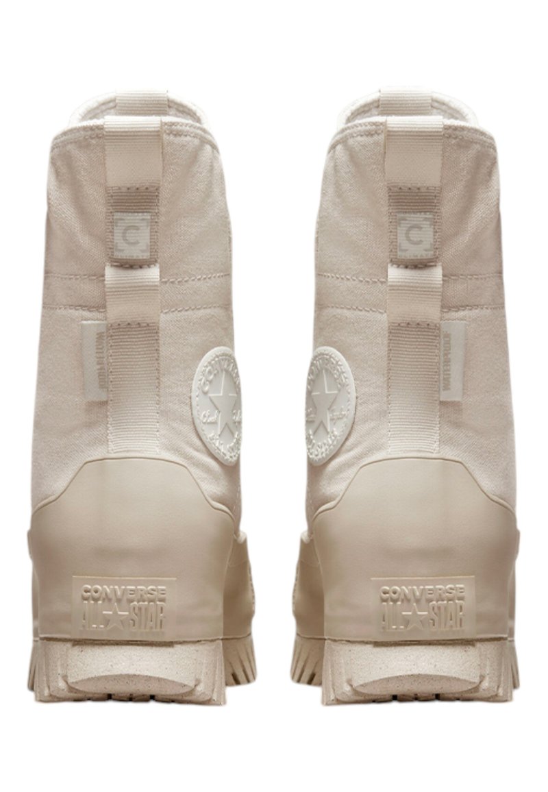 Beige Converse All Star Stiefel mit einem High-Top-Design, Obermaterial aus strukturiertem Stoff, Gummisohle und auffälligem, kreisförmigen Logo an der Ferse.