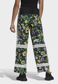 Blommönstrade byxor med svart bas, prydda med livfulla gröna, gula och lila blommor, vida ben och elastisk midja med vita detaljer.