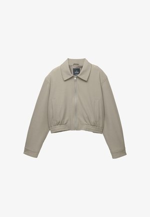 Veste cropped beige clair avec un col structuré, zip à l'avant et taille élastiquée. Dotée de deux poches latérales et de manches longues.