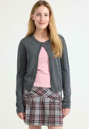 Cardigan grigio con bottoni, indossato sopra un top rosa, abbinato a una gonna a quadri con toni grigi, bianchi e bordeaux e lacci laterali.