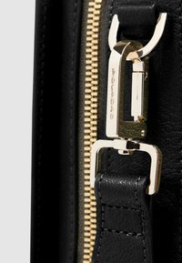 Detail van een zwarte leren tas met een gouden rits en metalen accenten. Zichtbare stiknaden en een getextureerde band verbeteren het ontwerp.