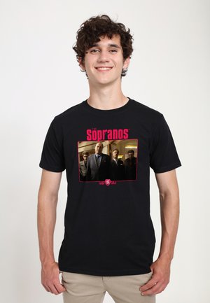 Jeune homme souriant portant un t-shirt noir avec une image en couleur et un texte rouge indiquant "The Sopranos".