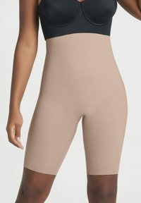 Beige vormgevende shorts van soepel, rekbaar materiaal, met een hoge taille en die tot halverwege het dijbeen reiken, ontworpen voor een naadloze pasvorm.