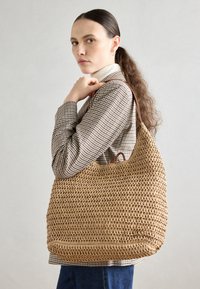 Wiklinowa torba na ramię w naturalnym kolorze o zaokrąglonym kształcie. Posiada skórzany pasek na ramię oraz otwarty wierzch ułatwiający dostęp.