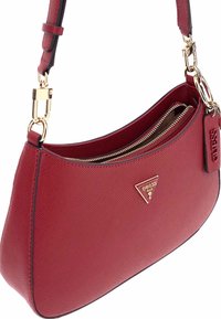 Borsa a tracolla rossa con texture, accentata da un logo dorato, chiusura con zip e tracolla rimovibile. Presenta una forma curva e bordi neri a contrasto.