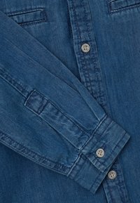 Camisa de mezclilla con tejido azul, dos bolsillos en el pecho, cierre de botones y mangas largas con puños abotonados. Acabado de algodón texturizado.