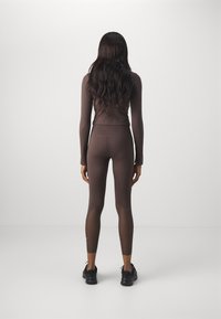 Completo da allenamento marrone composto da un top a maniche lunghe e leggings. I leggings presentano dettagli in rete e un design aderente. Scarpe sportive nere in vista.