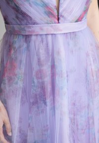 Lila Tüll-Kleid mit floralem Design in Pastellfarben. Der Stoff hat eine weiche Textur und wird an der Taille von einem passenden Satin-Gürtel gehalten.