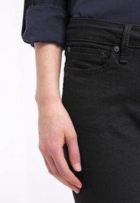 Vaqueros de mezclilla negra con cintura alta y diseño de cinco bolsillos, que presentan una textura suave y detalles de costura sutiles a lo largo de los bolsillos.