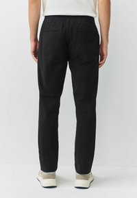 Black pants with a relaxed fit, elastic waistband, two back pockets, and a smooth fabric texture. Worn with light-colored sneakers.