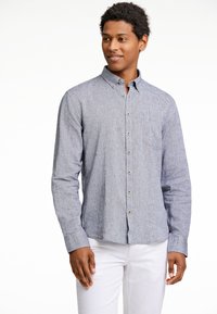 Lichtblauwe, knoopsluiting shirt van een gestructureerde stof met een borstzak. Het shirt heeft een kraag en lange mouwen, gecombineerd met witte broeken.