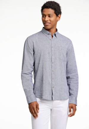 Lichtblauwe, knoopsluiting shirt van een gestructureerde stof met een borstzak. Het shirt heeft een kraag en lange mouwen, gecombineerd met witte broeken.