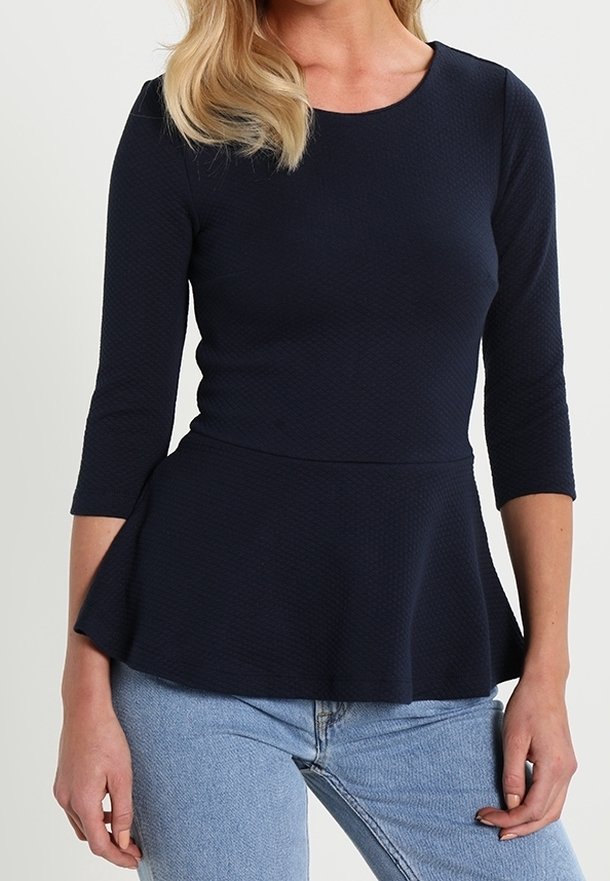 Navy Peplum-Oberteil mit 3/4-Ärmeln, texturiertem Stoff und rundem Halsausschnitt. Kombiniert mit hellblauen Jeans.