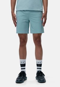 Gaiši zili sporta šorti ar elastīgu jostu, apvienoti ar melniem sporta apaviem un melnbaltām svītrainām zeķēm. Gluda tekstūra, līdz ceļgaliem garums.