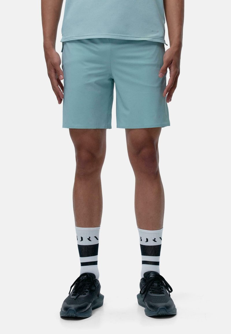 Gaiši zili sporta šorti ar elastīgu jostu, apvienoti ar melniem sporta apaviem un melnbaltām svītrainām zeķēm. Gluda tekstūra, līdz ceļgaliem garums.