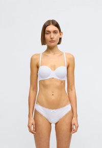 Fehér párnázott melltartó állítható pántokkal, fehér csipkés szegélyű bugyival párosítva. Simogató textúra és varrás nélküli kialakítás, minimális részletezéssel.