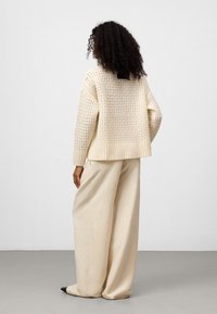 Crème gebreide trui met een openweefdesign en geribde zoom, gecombineerd met losse crèmekleurige broek en zwarte puntige schoenen.