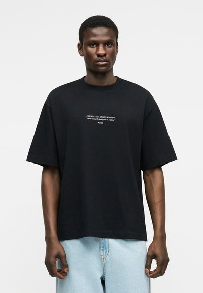 Άνδρας που φοράει μαύρο υπερμεγέθη μπλουζάκι με λευκό κείμενο "OFF-WHITE c/o VIRGIL ABLOH™ Κατασκευάστηκε στη γη, σχεδιάστηκε σε αεροπλάνο ©2013" και ανοιχτό μπλε τζιν.