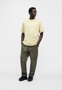 Ανοιχτό κίτρινο βαμβακερό t-shirt με κοντά μανίκια και στρογγυλή λαιμόκοψη, συνδυασμένο με χακί παντελόνι φαρδιάς γραμμής και μαύρα αθλητικά παπούτσια.