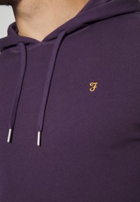 Felpa viola realizzata in morbido tessuto con una vestibilità slim. Presenta un piccolo logo dorato ricamato e punte metalliche argentate sui lacci.