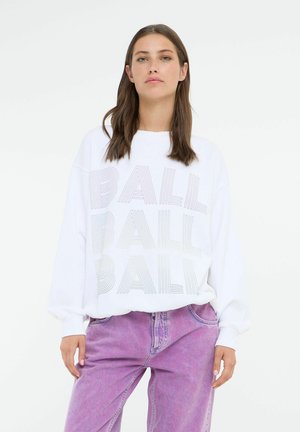 Hvid oversized sweatshirt med "BALL" trykt i multifarvede linjer; parret med lyserøde denimjeans med afslappet pasform.
