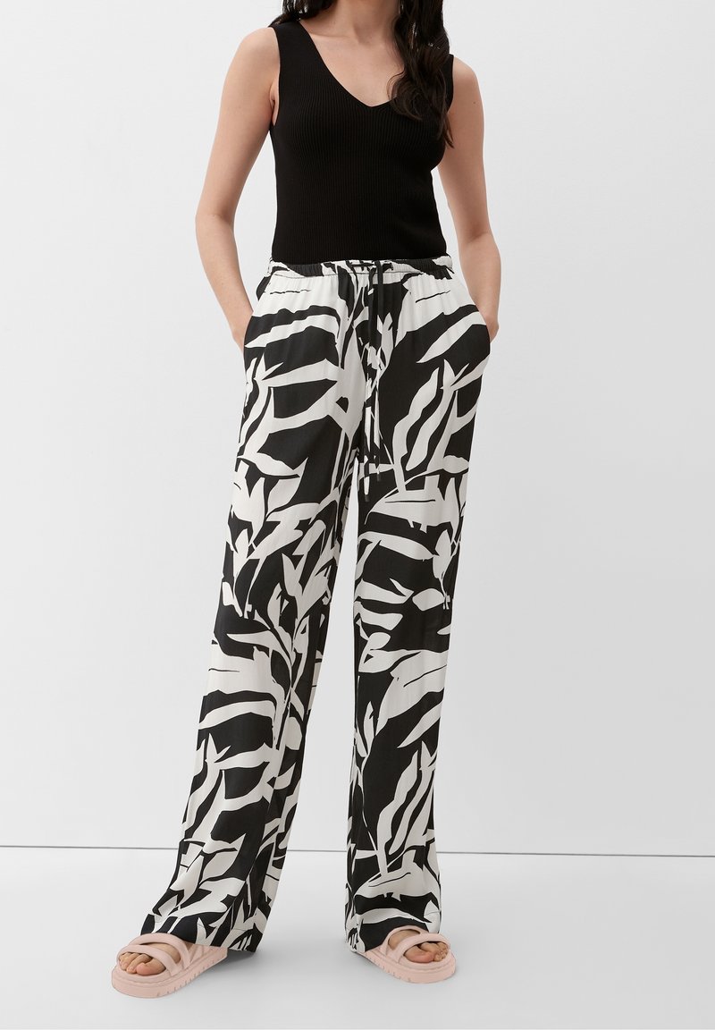 Pantalon à motif de feuilles en noir et blanc, coupe décontractée, taille à cordon, avec poches latérales, associé à un débardeur noir côtelé et des sandales.