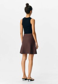 Jupe évasée marron en tissu doux, associée à un haut sans manches noir. Le design présente une texture lisse et une coupe au genou.