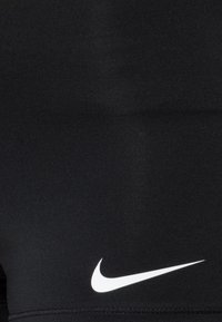 Svarta atletiska shorts gjorda av elastiskt tyg med en slät textur och en vit Nike-swoosh-logga på den nedre sidan.