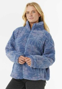 Veste en polaire bleu clair flou avec un col haut et une fermeture éclair, présentant un motif subtil, des manches oversized et une coupe décontractée.