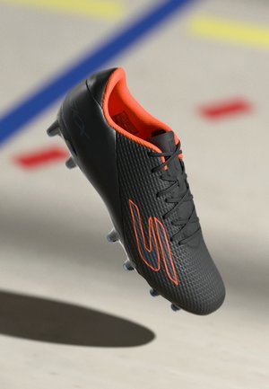 Black soccer cleat with a textured surface, bright orange interior, and laces. Features a prominent logo in orange on the side and molded studs.