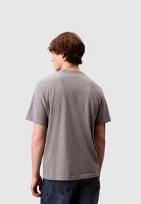 T-shirt grigia a maniche corte con vestibilità rilassata, scollo rotondo e tessuto morbido, indossata con jeans di denim blu, vista da dietro.