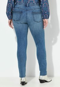 Jeans ajustados de color azul con una cintura de altura media, cinturilla elástica y dos bolsillos traseros. Combinados con botas de tobillo plateadas.