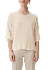 Beżowa, luźna bluzka z krótkimi rękawami i okrągłym dekoltem. Posiada białe wykończenie przy dekolcie i mankietach oraz miękką fakturę.