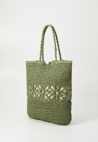 Groene gehaakte draagtas met een bloemen uitsnede ontwerp, voorzien van gevlochten handvatten en een gestructureerde stof. Open bovenkant zonder hardware.
