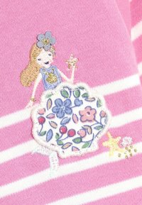 Broderad patch på rosa randig tyg föreställer en flicka med långt hår, blommig klänning, guldaccenter och stjärndetaljer.