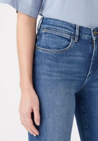 Jeans de denim azul claro con un diseño ajustado, que cuentan con bolsillos delanteros, detalles en dorado y una textura suave y desgastada.