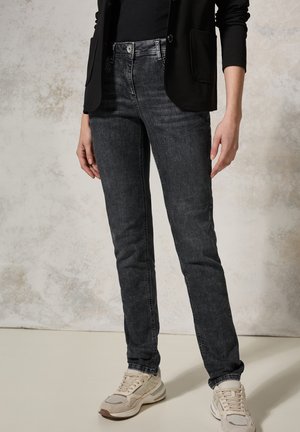 Slim-fit zwarte denim jeans met een licht vervaagde textuur, gecombineerd met lichtgekleurde sneakers en een zwarte blazer.