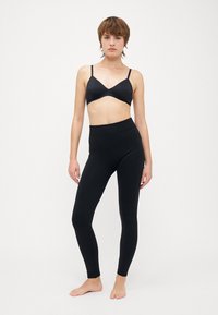 Schwarzer Sport-BH und hochgeschnittene Leggings aus glattem, dehnbarem Stoff. Merkmale ein einfaches Design und nahtlose Verarbeitung.