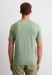 Light green short-sleeve t-shirt with a crew neck and a smooth texture. Features a tag at the back, paired with khaki pants.