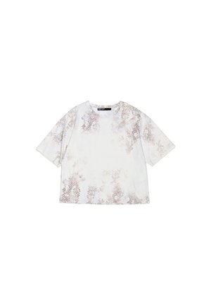Skrócony t-shirt wykonany z miękkiego materiału, z jasną białą bazą i brązowym abstrakcyjnym wzorem oraz krótkimi rękawami. Okrągły dekolt.