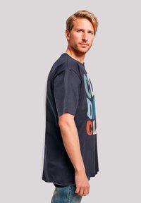 Navy cotton t-shirt with oversized fit featuring multicolored text "COLD DAY" and "CL" in bold capital letters. Short sleeves, round neckline.
