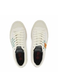 Une paire de baskets lacées blanc cassé avec des graphismes verts et oranges imprimés et des semelles noires, vues de dessus sur un fond blanc.