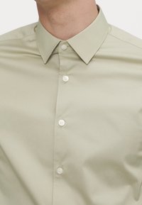 Uomo che indossa una camicia button-up beige chiaro con colletto a punte, visibile dal collo al petto.