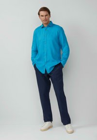 Helder turquoise linnen overhemd met knopen, marineblauwe broek en witte sneakers. Het overhemd heeft een gespreide kraag en een relaxte pasvorm.