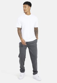 Witte T-shirt met korte mouwen, gecombineerd met donkergrijze joggingbroek en witte sneakers. De stof lijkt zacht en heeft een losse pasvorm.