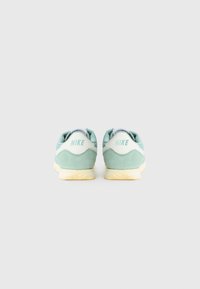 Nike tenisice imaju gornji dio od mint zelene suede kože, bijele kožne detalje i žutiju gumenu potplatu. Na peti je istaknuto ime brenda u svijetloplavoj boji.