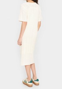 Knee-length, lyhythihainen kermaisen värinen mekko, jossa on tekstuurilliset neulekuviot. Yhdistettynä rentoihin tennareihin, joissa on vihreät raidat ja korkea pohja.