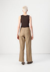 Top senza maniche marrone, pantaloni beige a vita alta con due tasche posteriori e scarpe nere con motivo animalier.