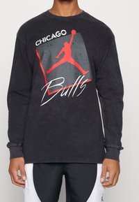 Långärmad svart t-shirt med en grafisk design som visar en röd silhuett av en basketspelare och texten "Chicago Bulls" i vit font.